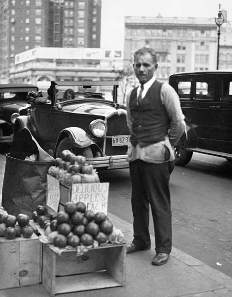 1930s SIDEWALK APPLE VENDOR MAN LOOKING AT CAMERA DURING THE GREAT DEPRESSION