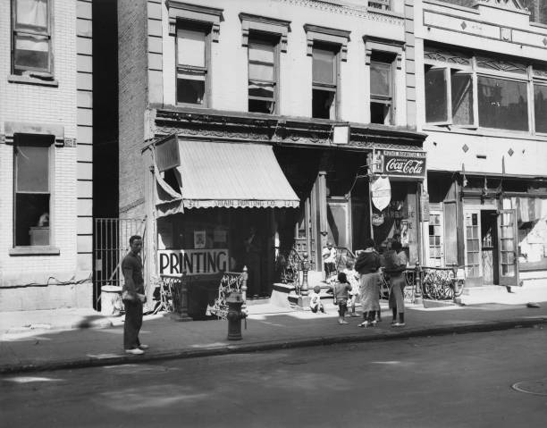 New Yorkers on the sidewalk outside a shop advertising printing part of a tenement building in Harlem New York City New York 16th October 1935.