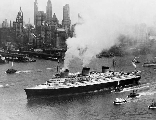 Tugboats follow alongside the French turbine-electric ocean liner SS Normandie as it travels through New York Harbor.