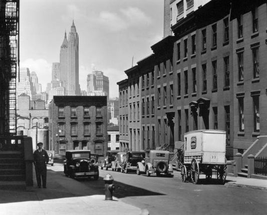 1930s New York City - Laundry wagon cars along sloping street lined with rowhouses skyline of Manhattan visible above buildings at end of the