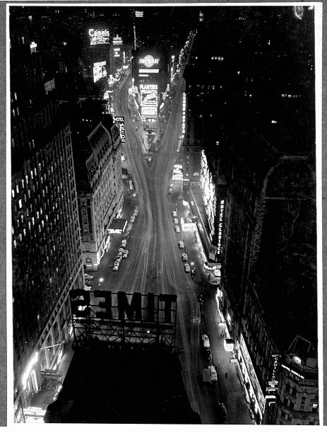 Advertising signs light the bases of office buildings and skyscrapers in Times Square Canyon at Night New York City by Vincent Lopez. Ca. 1937.