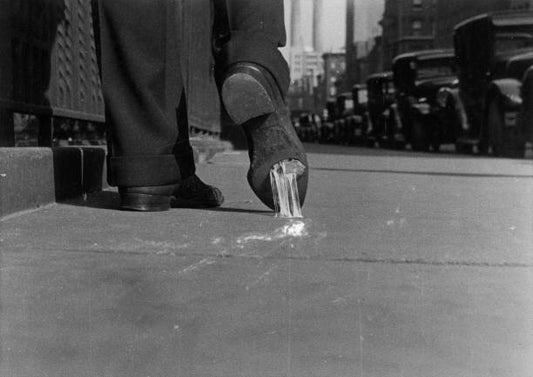 Close-up view of a man walking on a city sidewalk with chewing gum stuck on the bottom of his shoe New York 1930.