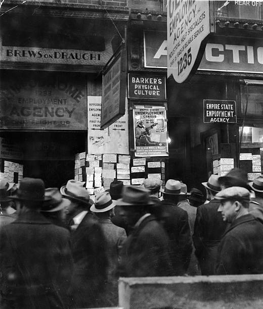 Crowed of unemployed men gather in the rain in front of a row of employment agencies on Sixth Avenue during the Great Depression New York City 1931.
