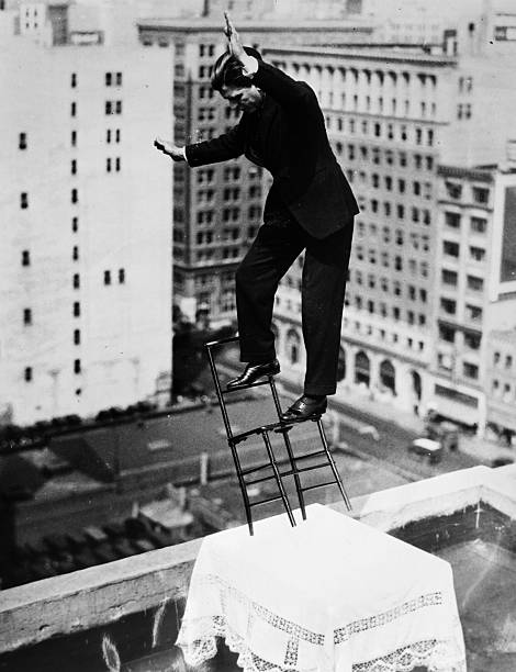 French equilibrist Gilbert Bettancourt tests his balance on a chair resting on a table with only two legs close to the edge of the building roof on