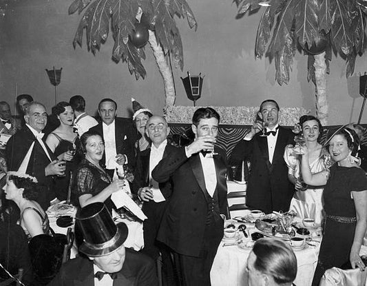 Group of men and women smile at the camera raising and sipping their glasses of champagne at the stroke of midnight on New Year's Eve at the El