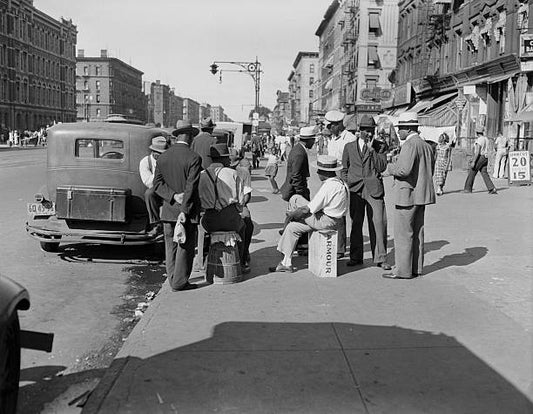 Group of men converse on a sidewalk on busy Lenox Avenue in Harlem New York City on an summer afternoon.