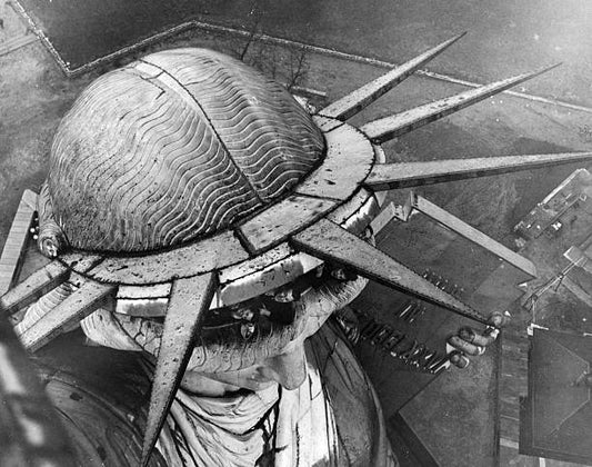 Group of people leaning out of the head of the Statue of Liberty in New York seen from the torch above.