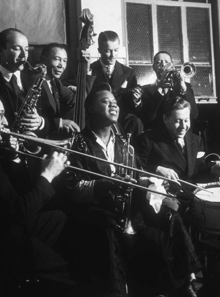 Group portrait of American jazz musician Louis Armstrong and his orchestra during a jam session at the Paramount Theater in New York City. Front row