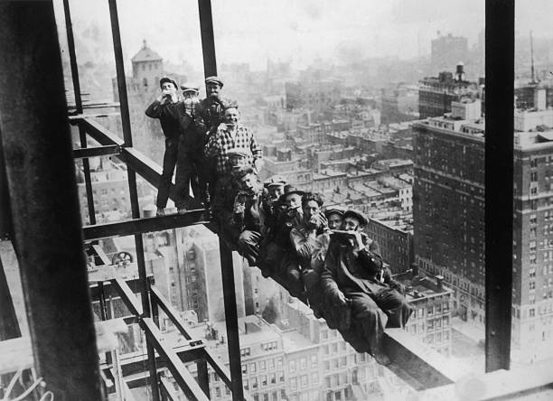 Harmonica playing steel workers perched on a girder on the 22nd storey of the Murray Hill building New York.