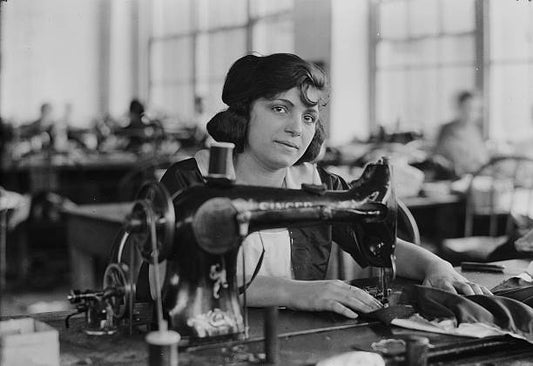 Italian woman looks up from her work as she sews clothing in an unidentified factory possibly in New York city ca.1930.