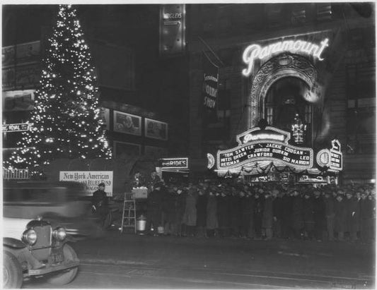 Nighttime view of New York American Christmas and Relief Fund Lunch Wagon next to lighted Christmas tree and crowd of men; in front of the Paramount