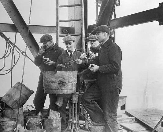 Noon hour on the top of the mooring mast and tower of the gigantic Empire State Building rising on the site of the old Waldorf. Men toasting their