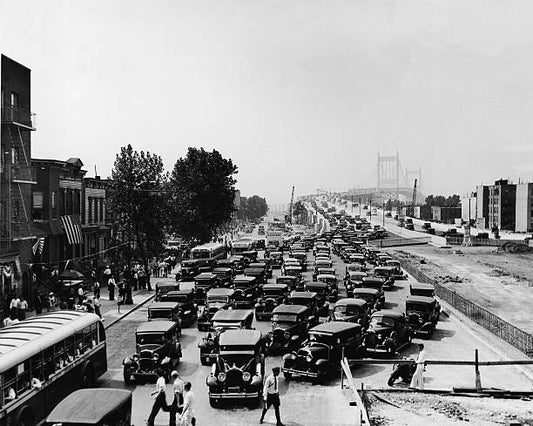 Pedestrians walk on the sidewalk and cross in front of cars exiting the Triborough Bridge in Harlem New York New York 1936.