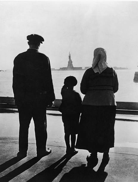Rear view of an immigrant family on Ellis Island looking across New York Harbor at the Statue of Liberty 1930s.