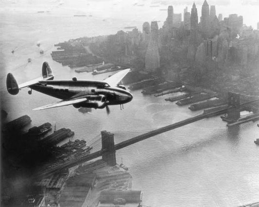 Twin-propeller Lockheed 14 Super Electra flies over down town Manhattan and the Brooklyn Bridge New York City. Inside American millionaire Howard