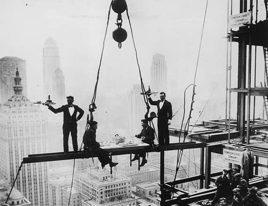 Two waiters serve two steel workers lunch on a girder high above New York City 14th November 1930. The building upon which they are perched is the