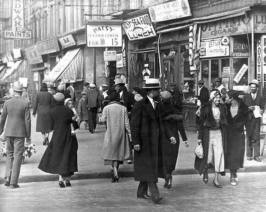 View of pedestrians on an unspecified street as they pass various shops in the Harlem neighborhood New York New York 1930s.