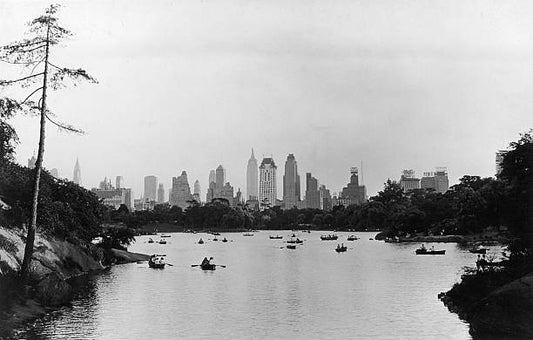 View of the midtown Manhattan skyline from the lake in Central Park with people in rowboats on the water New York City. The Empire State Building